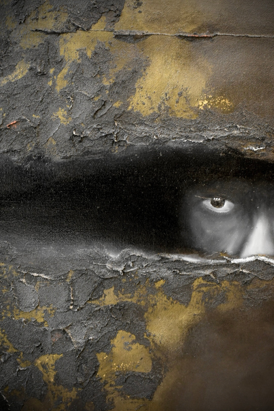 Abstract textured artwork with a dark horizontal band across the center and a partially visible human eye on the right side, set against cracked black, gray, and gold surfaces.