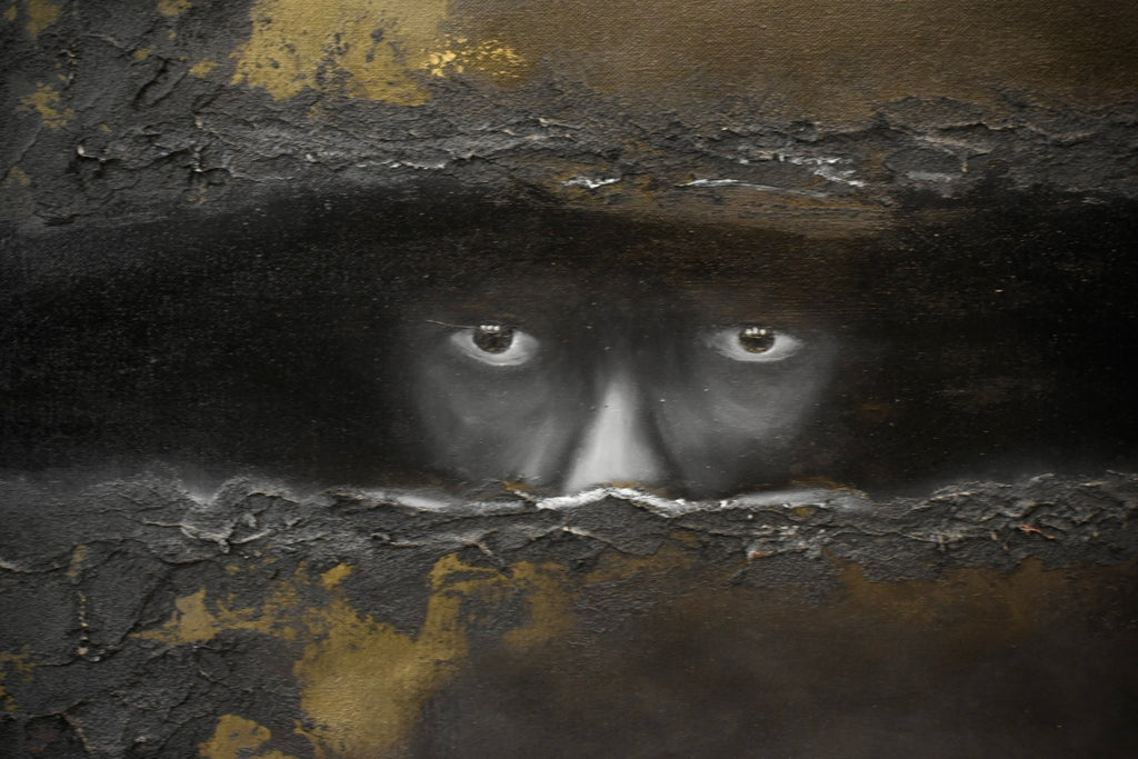 A dark, textured artwork depicting a human face peering through cracked black and gold plaster-like surfaces, with the eyes and nose area most prominent.