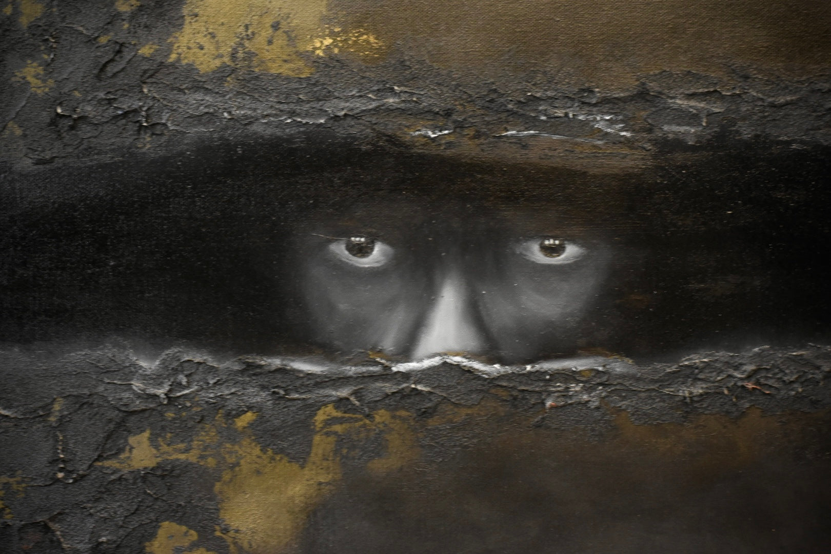 A dark, textured artwork depicting a human face peering through cracked black and gold plaster-like surfaces, with the eyes and nose area most prominent.