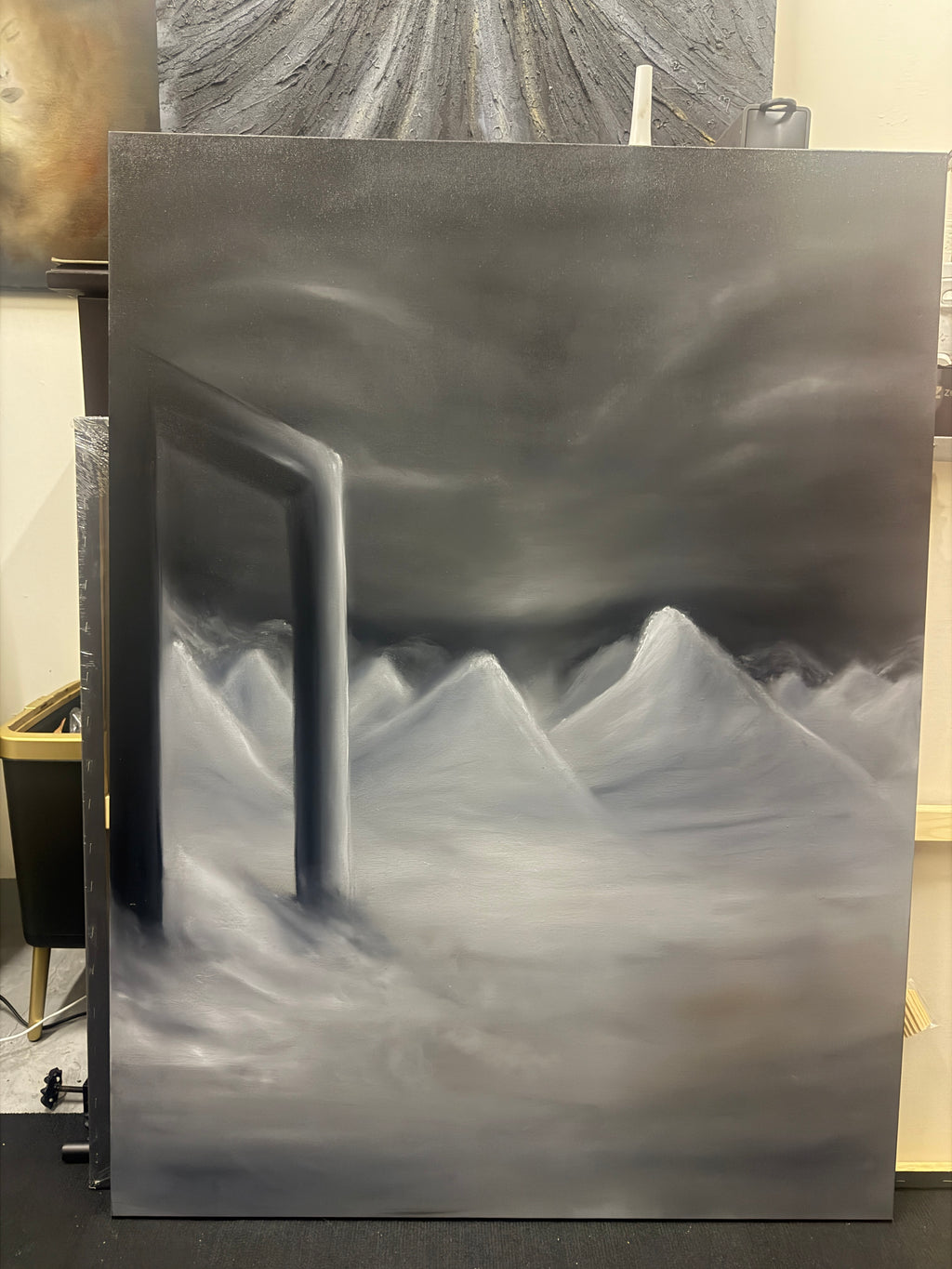 A large rectangular canvas painting featuring an abstract desert canyon scene with white sand dunes and dark gray shadows, photographed from above in what appears to be a studio or gallery space.