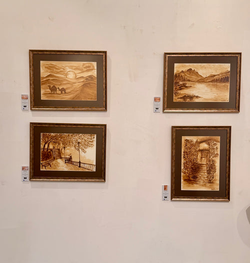 Gallery view of four framed coffee paintings by Cristina Gabriela Buzatu displayed on a white wall, including desert camel scene, mountain lake, park promenade and garden doorway